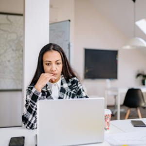 Young professional woman pausing at her laptop, appearing reflective or stressed in an office setting.